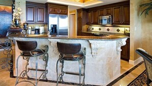 A spacious kitchen with dark wooden cabinets, a central island with bar stools, stainless steel appliances, and decorative elements. - MAISON PAR LEAU 3 Bedroom Holiday Home by Five Star Properties (Destin)