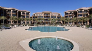 A hotel with a swimming pool and a fountain, surrounded by palm trees and lounge chairs. - MEDITERRANEA 401A 3 Bedroom Holiday Home by Five Star Properties (Miramar Beach)