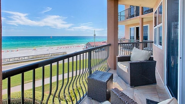 A balcony with wicker furniture, a view of the beach, and a clear sky. - MEDITERRANEA 401A 3 Bedroom Holiday Home by Five Star Properties (Miramar Beach)