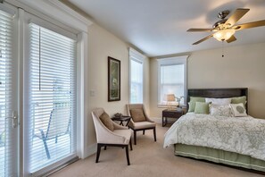 A bedroom with a bed, two chairs, a nightstand, a ceiling fan, and large windows with blinds. - MIRAMAR BEACH VILLAS 103 4 Bedroom Holiday Home by Five Star Properties (Miramar Beach)