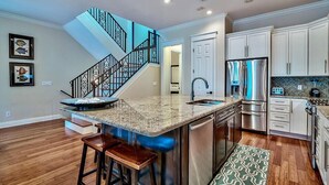 A modern kitchen with a central island, stainless steel appliances, and a staircase with a black railing. - Ocean Escape 4 Bedroom Holiday Home by Five Star Properties (Destin)
