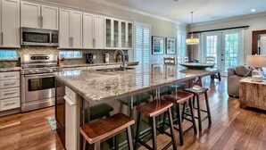 A modern kitchen with white cabinets, stainless steel appliances, and a large island with stools. - Ocean Escape 4 Bedroom Holiday Home by Five Star Properties (Destin)