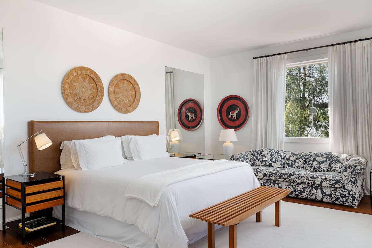 Un dormitorio con cama, mesitas de noche, un banco, un sofá y platos decorativos en la pared.
