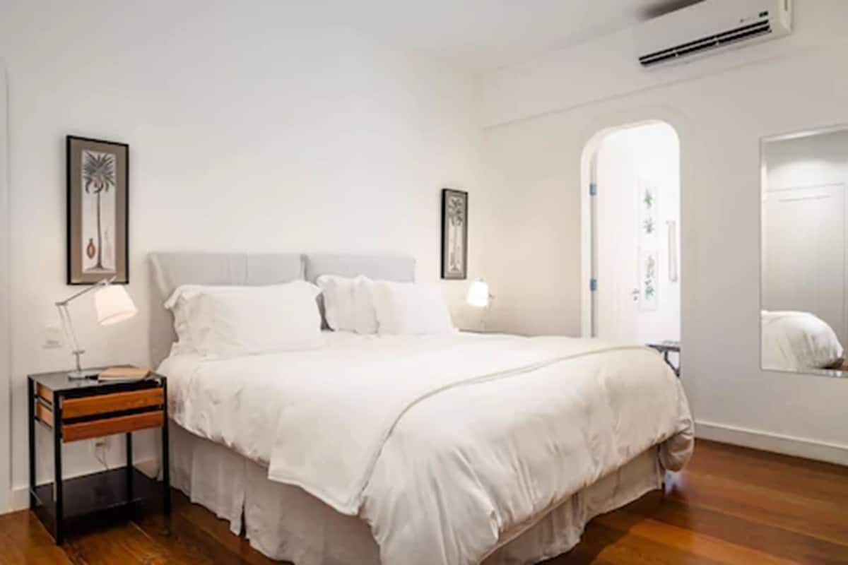Un dormitorio con cama, mesitas de noche, un espejo y cuadros en la pared.