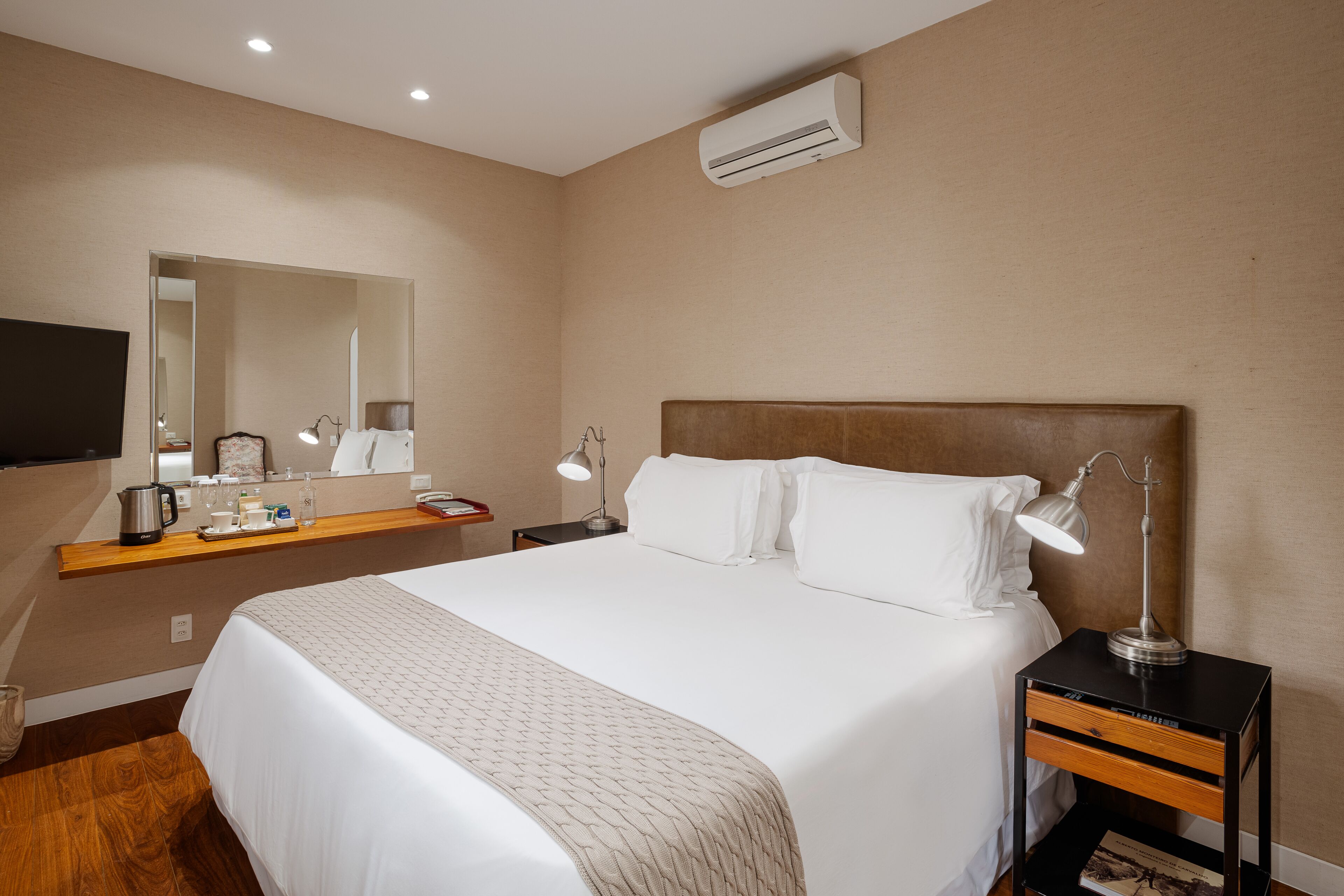 A hotel room with a large bed, a nightstand with a lamp, a mirror, and a flat-screen TV.