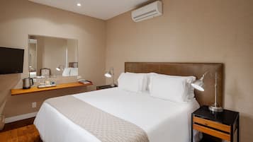 A hotel room with a large bed, a nightstand with a lamp, a mirror, and a flat-screen TV.