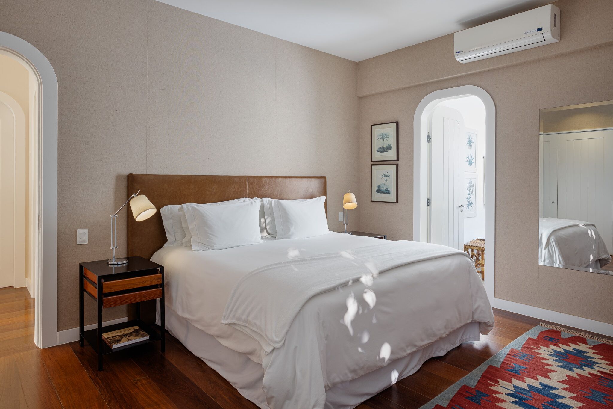 A bedroom with a wooden headboard, white bedding, a nightstand with a lamp, and a patterned rug.
