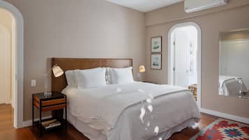 A bedroom with a wooden headboard, white bedding, a nightstand with a lamp, and a patterned rug.