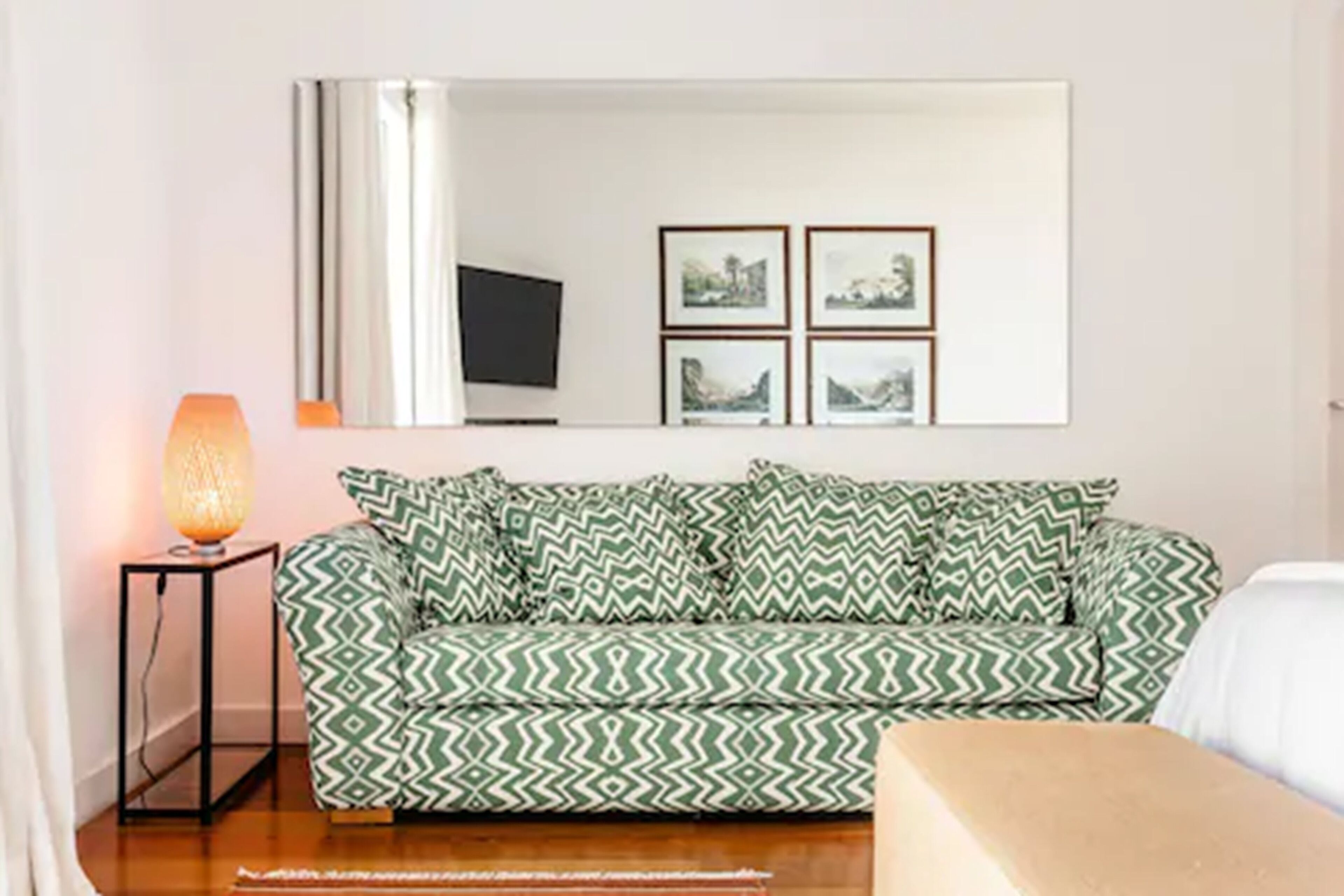 Un salon avec un canapé à motifs, une table d’appoint avec une lampe, un téléviseur à écran plat et des tableaux encadrés accrochés au mur.