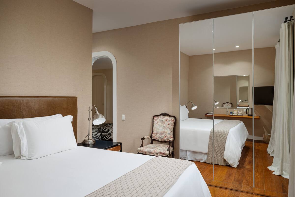 Una habitación de hotel con una cama grande, una silla, un escritorio con lámpara y un espejo.