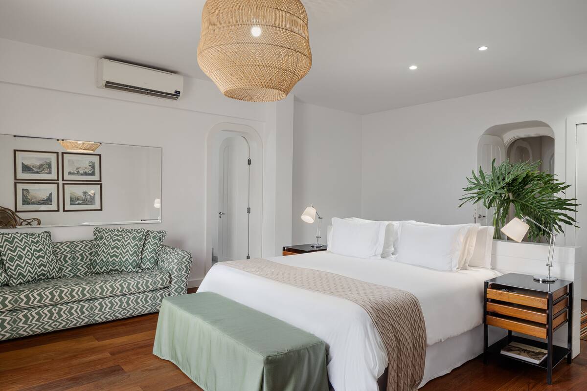 Un dormitorio moderno con una cama grande, mesitas de noche, un sofá verde y una planta grande.