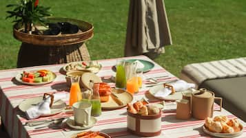 A picnic setup with a table covered by a striped tablecloth, featuring plates of food, drinks, and a basket of bread.