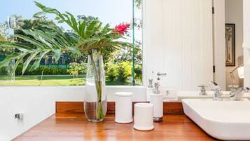 Une salle de bain moderne avec un meuble-lavabo en bois, un grand lavabo blanc et un vase contenant des plantes vertes et une fleur rouge.