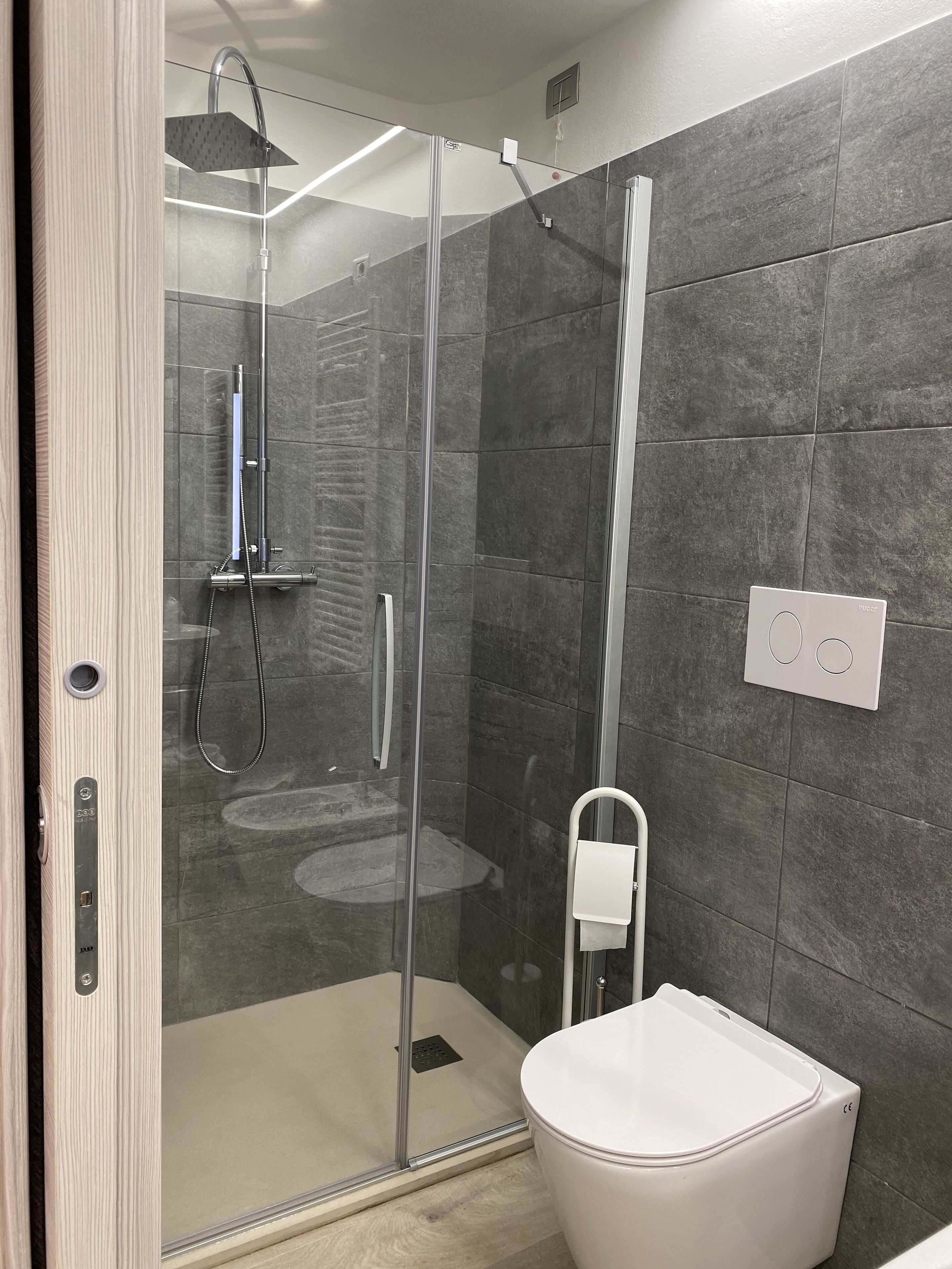 Ein modernes Badezimmer mit einer gläsernen Duschkabine, einer weißen Toilette und grauen Fliesenwänden.