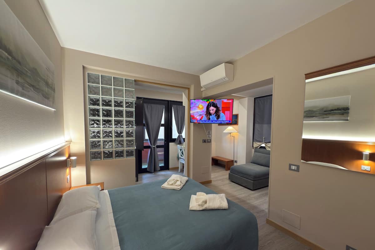 A hotel room with a bed, a television, a seating area, and a view of the outside.