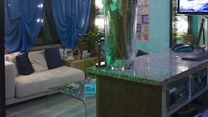 A modern living room with a sofa, a coffee table, a TV, and a decorative plant arrangement. - Hotel Rinaldo Apartments (Borgomanero)