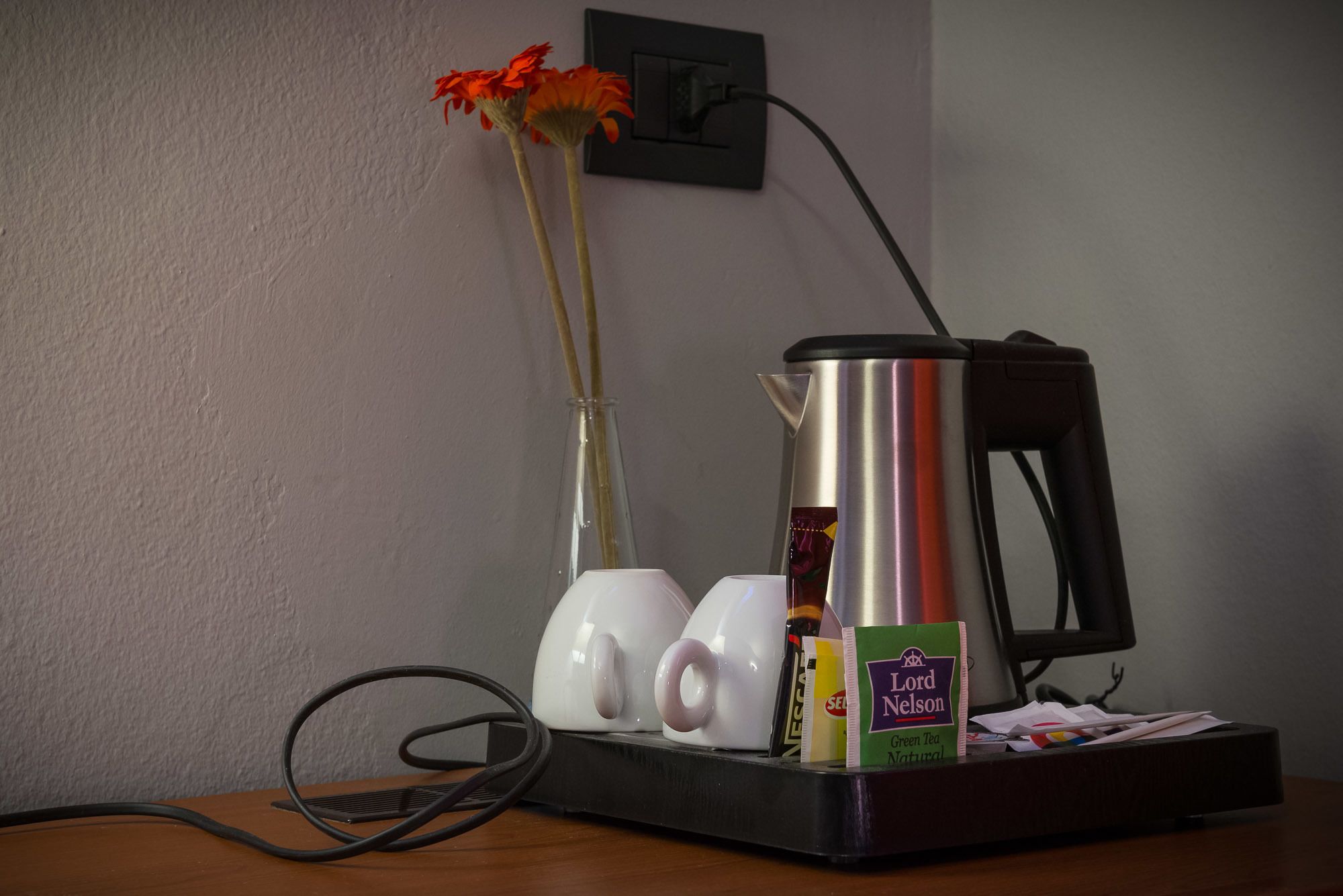 A coffee maker, a vase with flowers, and a tea bag on a table.