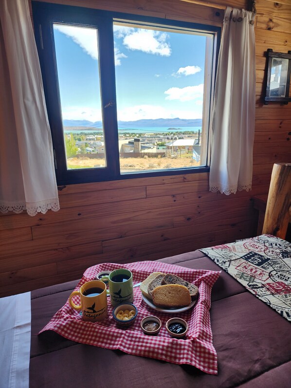 A cozy room with a large window overlooking a scenic landscape, a checkered tablecloth, and a variety of breakfast items.