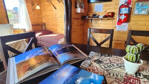 A cozy wooden cabin interior with a dining table, books, a cactus, and a mounted television. - Cabañas Alechen (El Calafate)