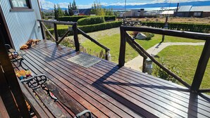 A wooden deck with a view of a green landscape and distant buildings. - Cabañas Alechen (El Calafate)