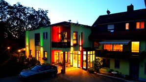 A two-story building with a balcony and a car parked in front. - Rothsee Hotel (Allersberg)