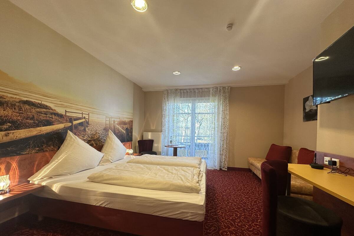 A hotel room with a bed, a desk, a chair, a television, and a window with curtains.