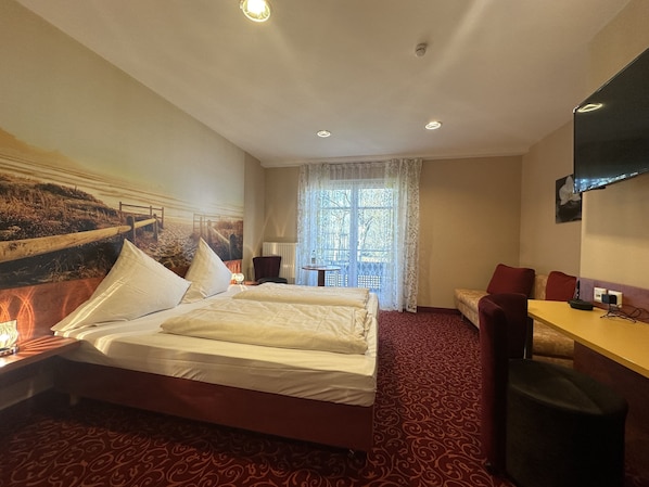 Una habitación de hotel con cama, escritorio, silla, televisión y ventana con cortinas.
