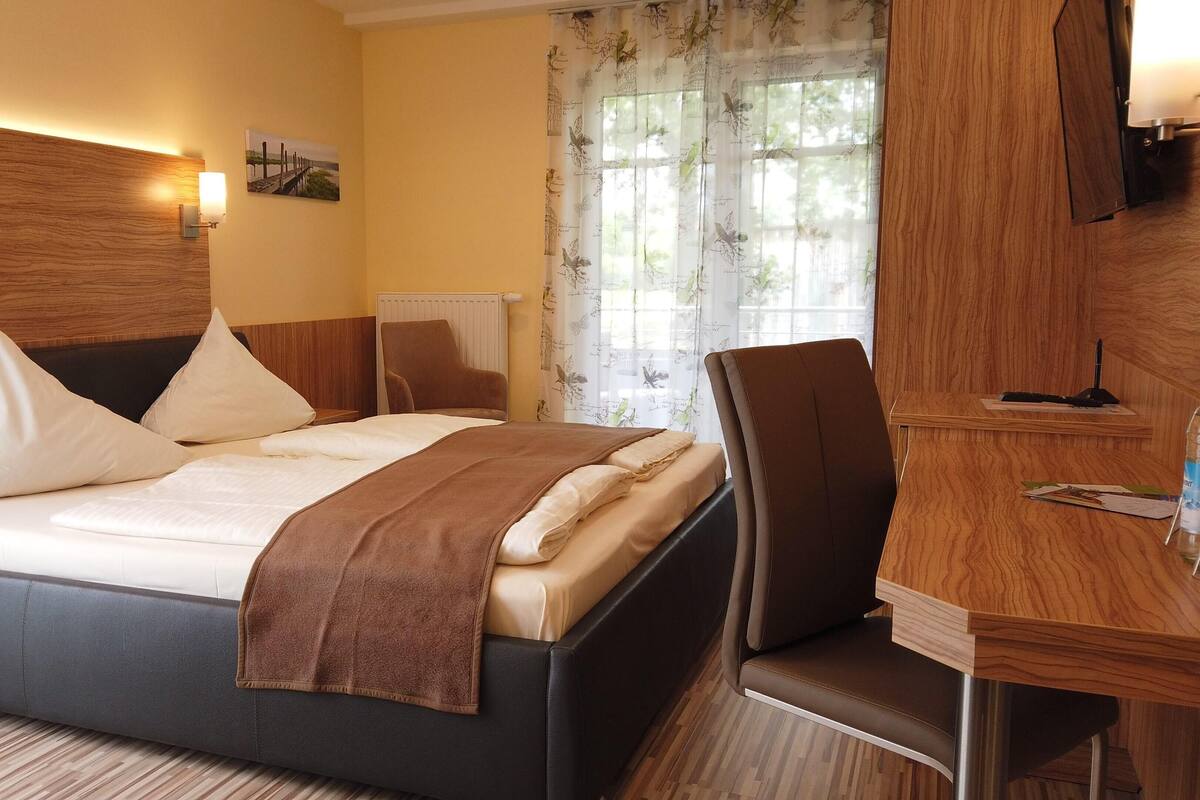 A hotel room with a bed, a desk, a chair, a lamp, and a window with curtains.
