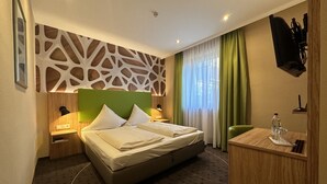 A hotel room with a bed, bedside tables, a desk, a chair, a TV, and a window with curtains. - Rothsee Hotel (Allersberg)