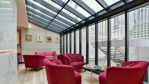 Un interior moderno con sillas tapizadas en rojo, un techo de cristal y obras de arte en las paredes.