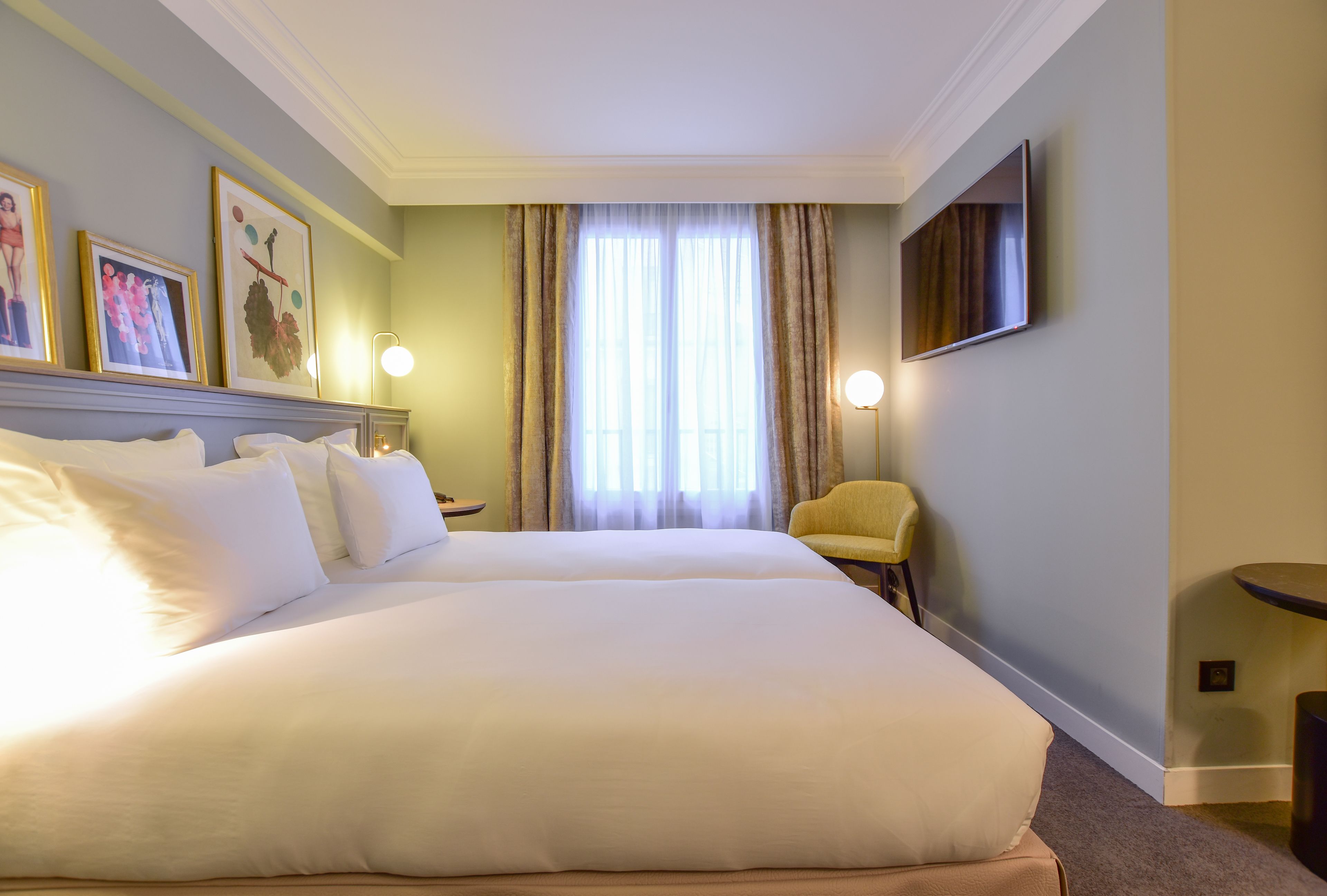 Een hotelkamer met een groot bed, een stoel, een televisie en ingekaderde foto's aan de muur.