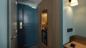 Un pasillo con una puerta azul, un armario de madera, una lámpara en la pared y una pequeña mesa con una tableta.