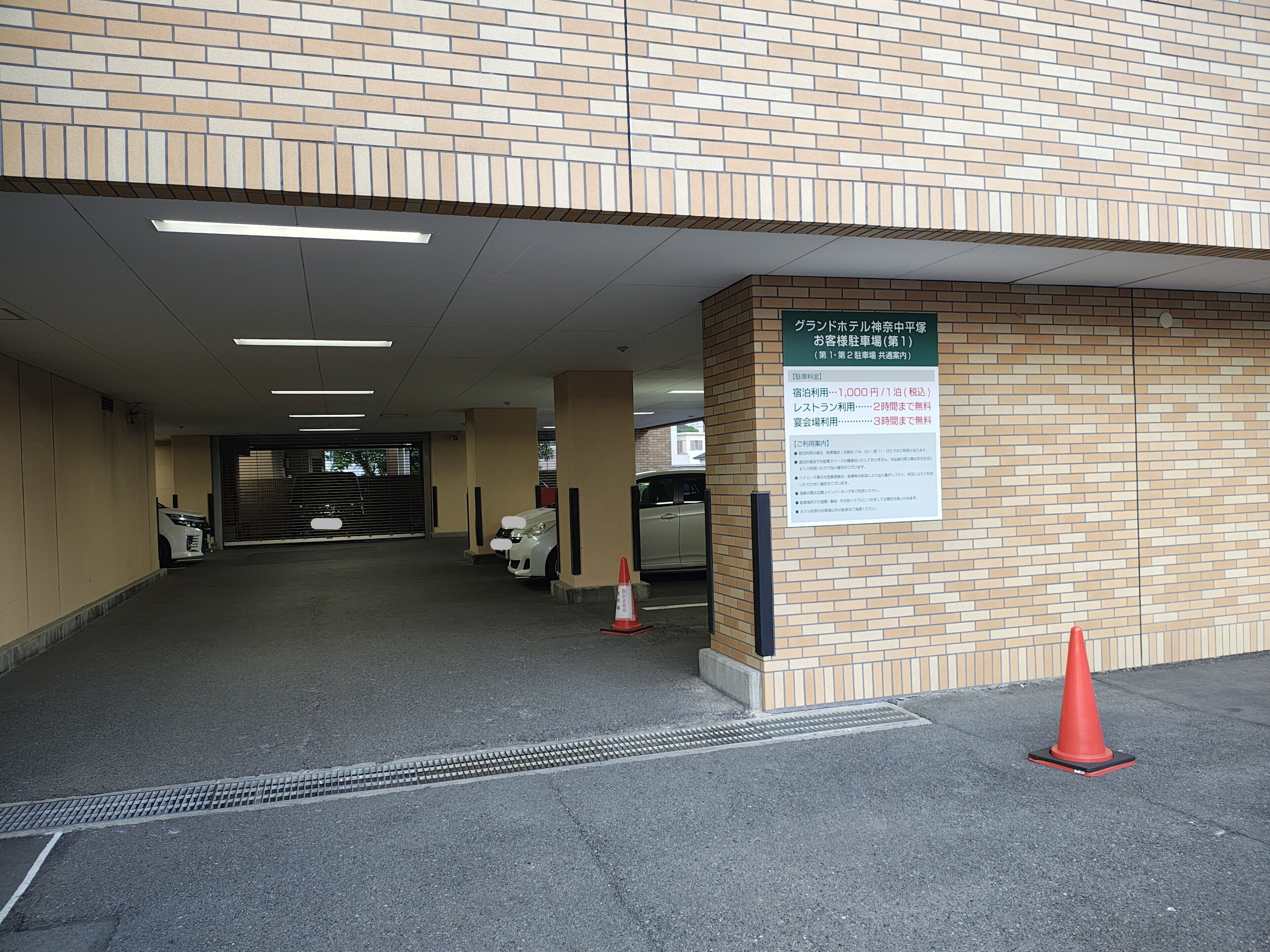 A parking garage entrance with a brick wall, a signboard, and a few parked cars.