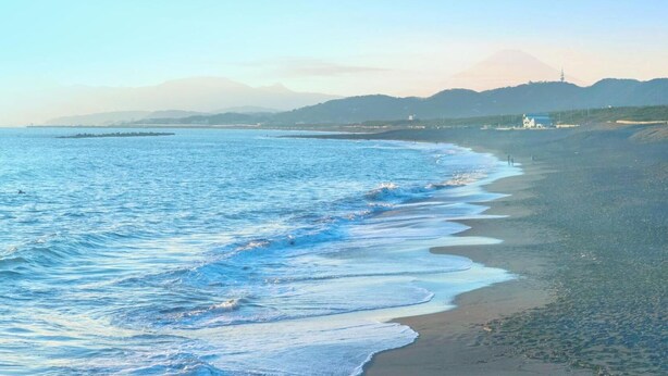 Platja amb onades, una muntanya allunyada i cel serè.