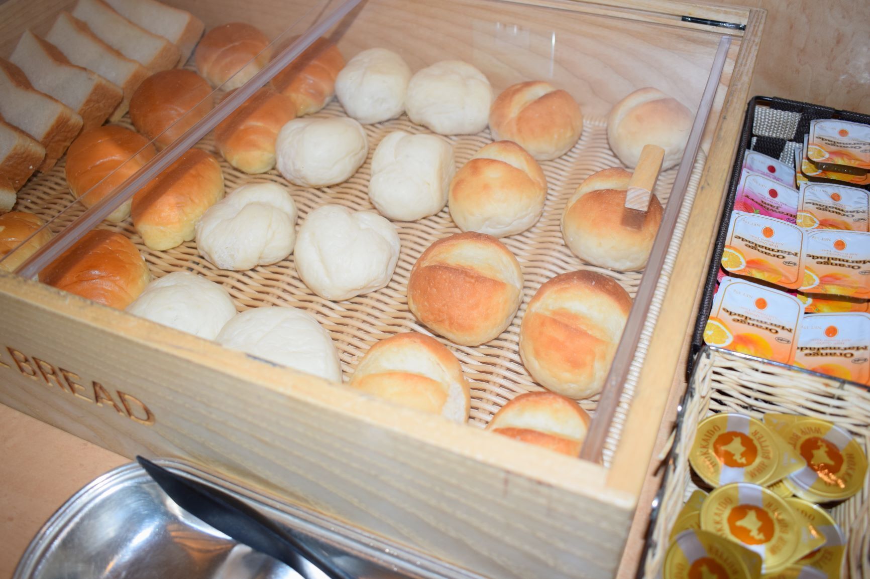 A display case with various baked goods, including bread rolls and buns, and a selection of packaged snacks.