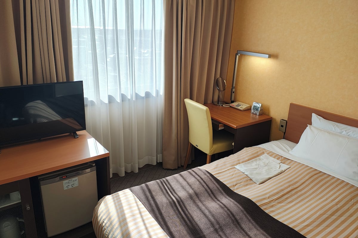Habitación de hotel con cama, escritorio con silla, televisor, teléfono y lámpara.