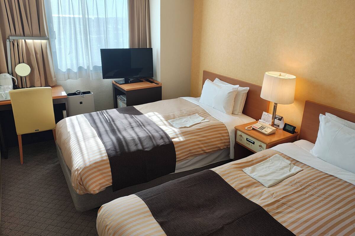 Una habitación de hotel con dos camas, un escritorio con computadora, un televisor y una lámpara.