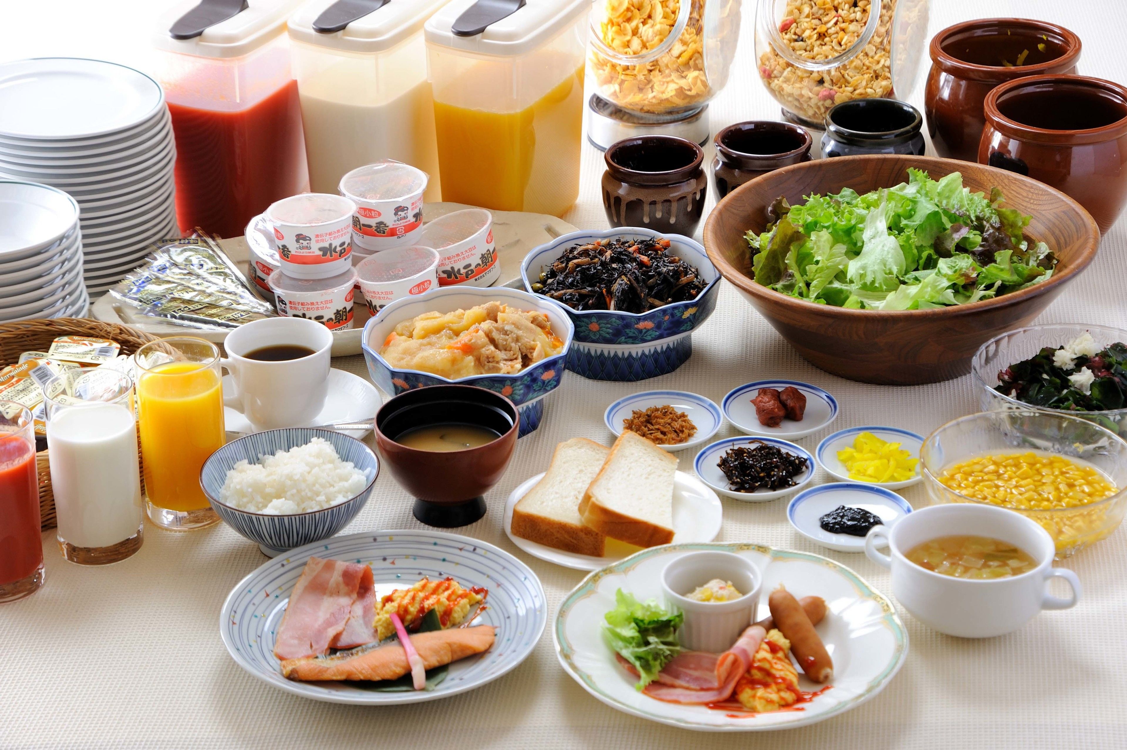 A table with various breakfast items including bowls of soup, plates of eggs, toast, and a large salad.