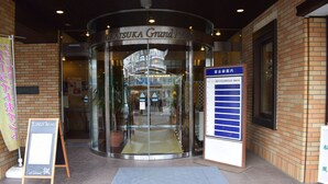 Entrada a l'Hotel Hiratsuka Grand amb una porta giratòria de vidre, un cartell i un menú a la pissarra a l'exterior.