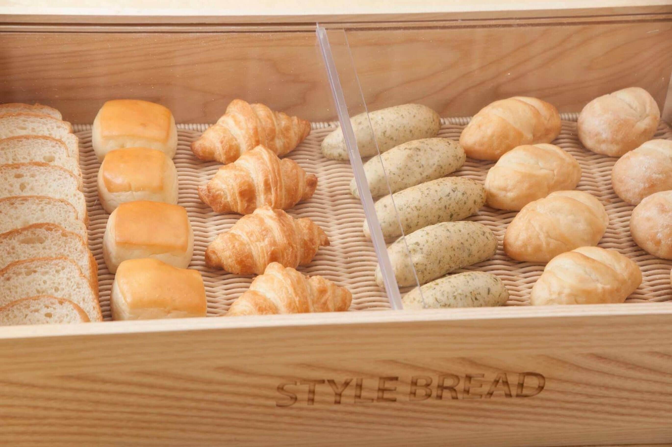 Ein Holzbrotkasten mit der Aufschrift „STYLE BREAD“, gefüllt mit verschiedenen Brotsorten, darunter Brötchen, Croissants und Baguettes.