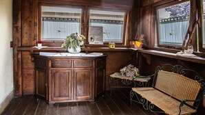 A wooden cabin interior with a wooden cabinet, wicker bench, and a small table with a basket of flowers. - Agriturismo Tre Rondini (Legnago)