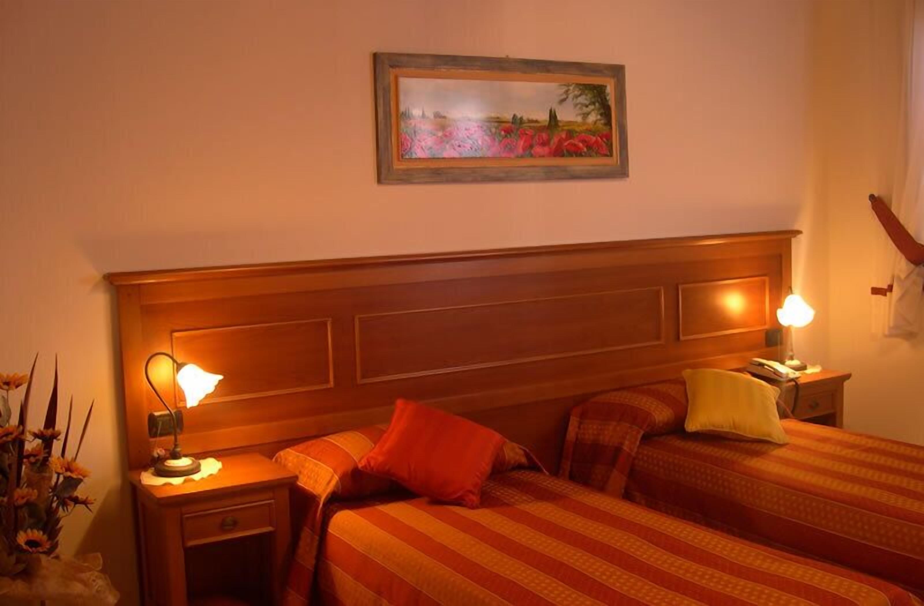 Une chambre d’hôtel avec une tête de lit en bois, deux tables de chevet avec des lampes, un lit avec une literie à rayures et un tableau accroché au mur.