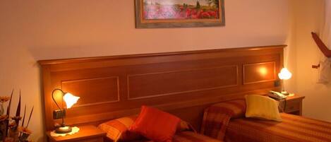 Une chambre d’hôtel avec une tête de lit en bois, deux tables de chevet avec des lampes, un lit avec une literie à rayures et un tableau accroché au mur.