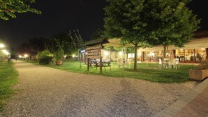 A gravel path leading to a building with outdoor seating and a sign indicating amenities like agriculture, wine, and food. - Agriturismo Tre Rondini (Legnago)