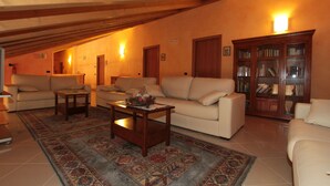 A cozy living room with a high ceiling, a fireplace, a sofa, a coffee table, and a bookshelf. - Agriturismo Tre Rondini (Legnago)
