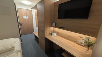 Una habitación de hotel con una cama, un escritorio con televisor, un armario de madera y un pequeño banco.
