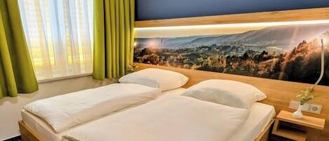 A double bed with a wooden frame, a nightstand with a lamp, and a view of a mountainous landscape through a window with green curtains.