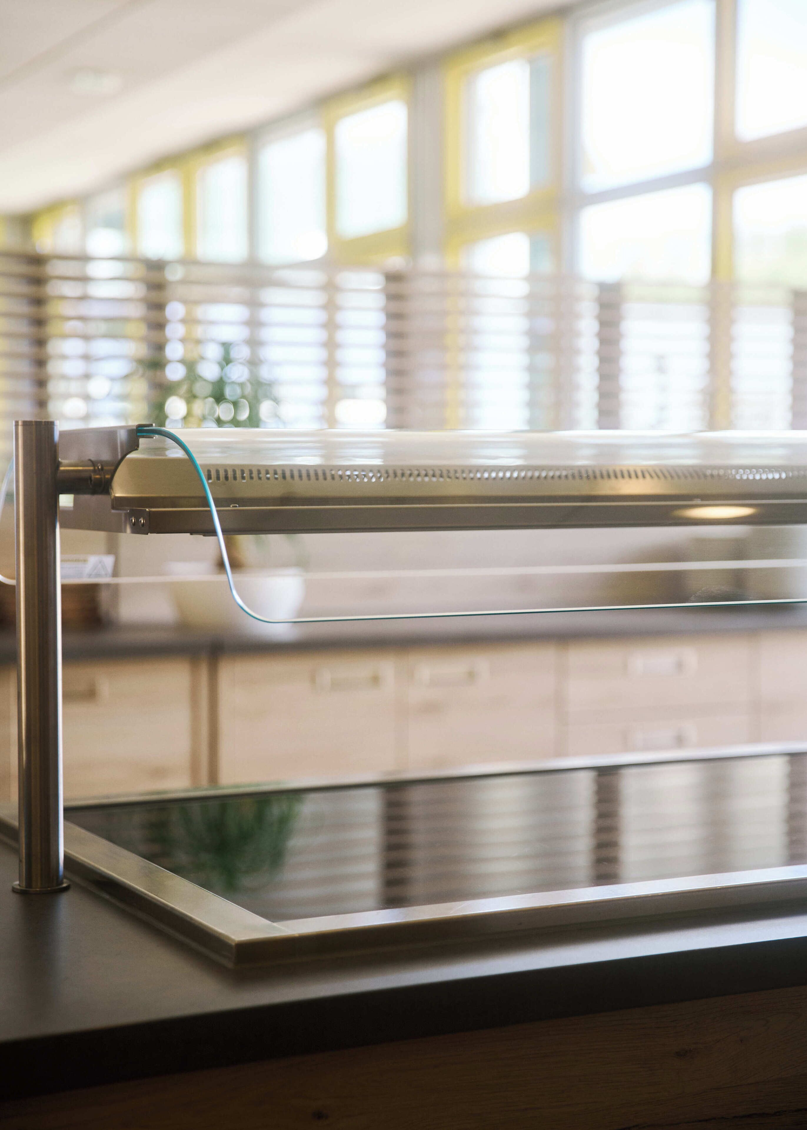 A kitchen counter with a stainless steel appliance, a window with blinds, and a view of the outside.