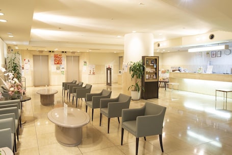 A hotel lobby with seating areas, a reception desk, and informational posters on the walls.. Grand Hotel Kanachu Hadano