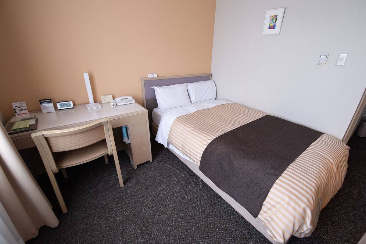 A hotel room with a bed, a desk, a chair, a telephone, and a small table.
